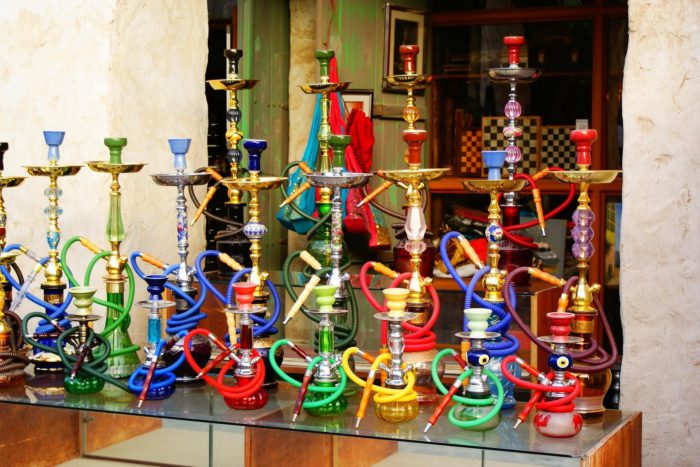 Colourful display of assorted shisha pipes with vibrant glass bases and coiled hoses arranged outside a shopfront.
